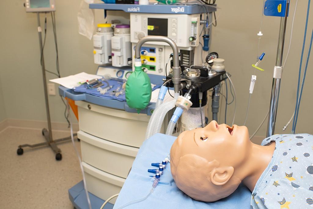 a patient simulator lies on a bed in a clinical simulation room